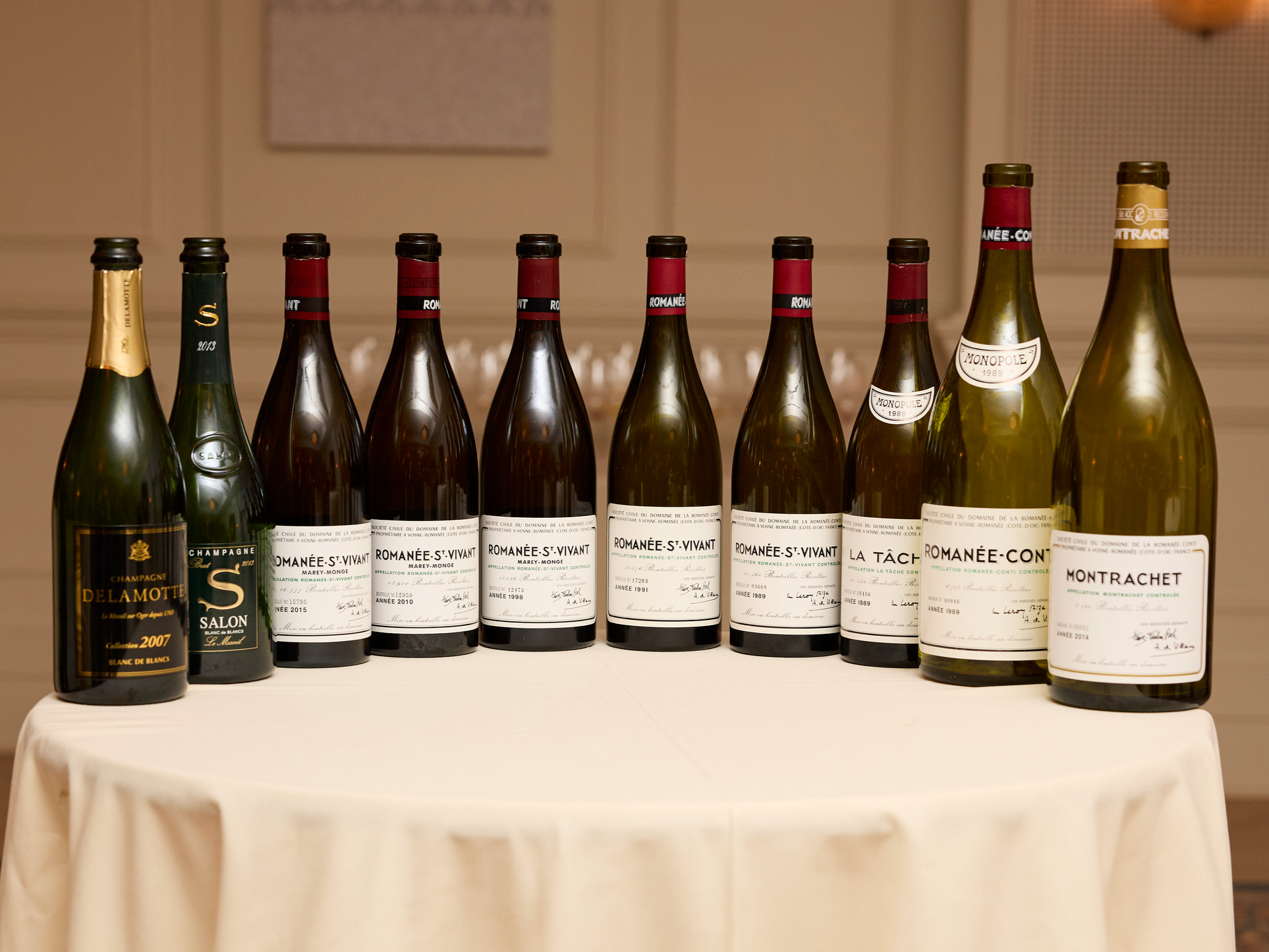 Ten wine bottle lineup from The Legends Dinner at La Paulée NYC 2025  with labels including Romanée-Conti and Montrachet are arranged on a round table with a white tablecloth in a softly lit room.
