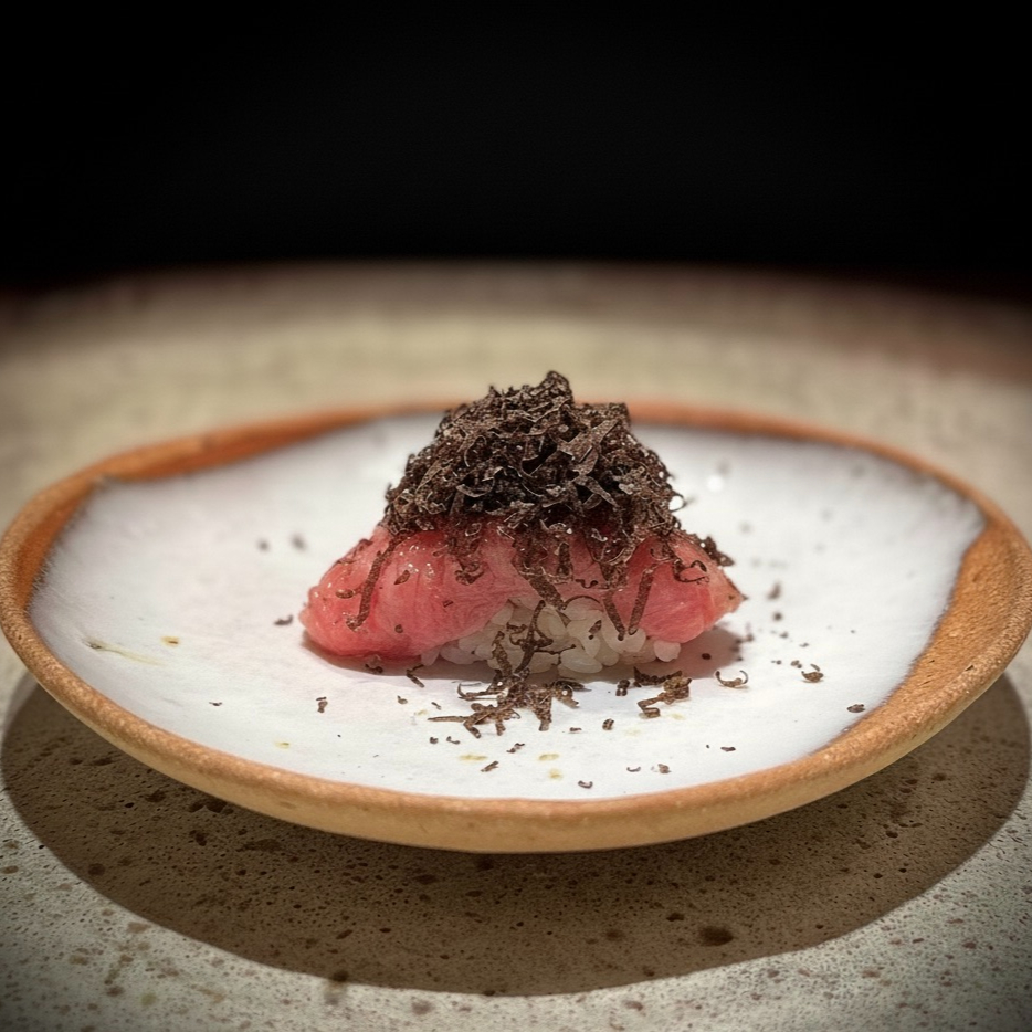 Sushi topped with thinly sliced truffles on a white plate with a brown rim, set against a dark background, exuding an elegant, gourmet vibe.