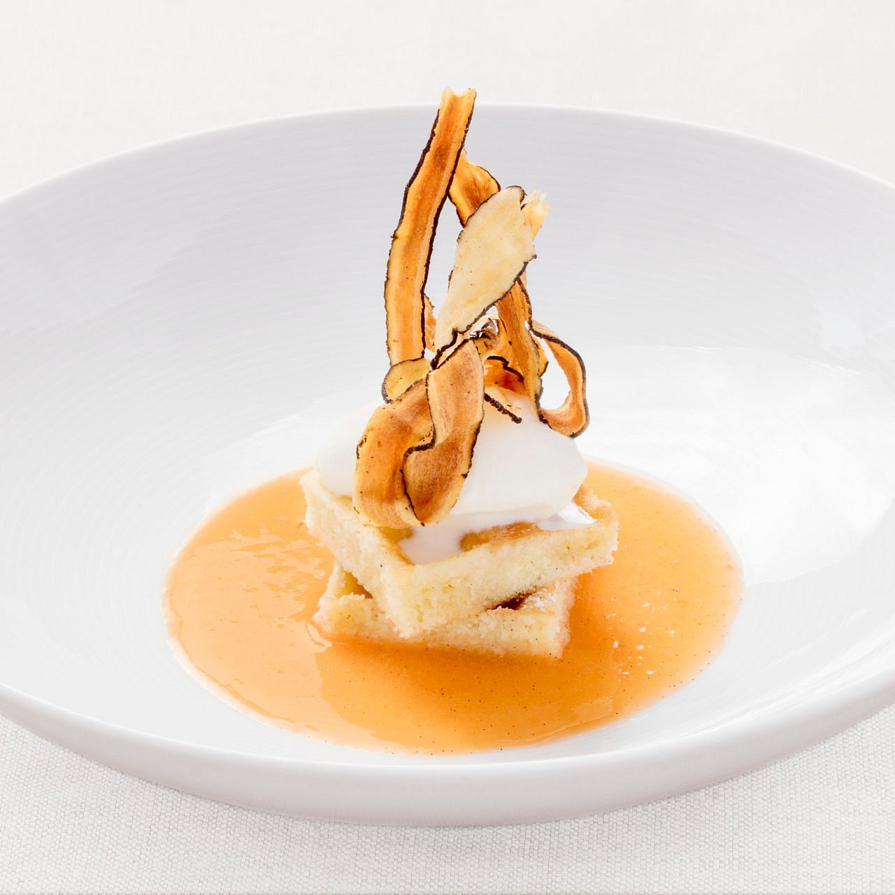 Elegant dessert with layered cake, whipped cream, and caramelized apple slices on a white plate. Light sauce surrounds the stack.