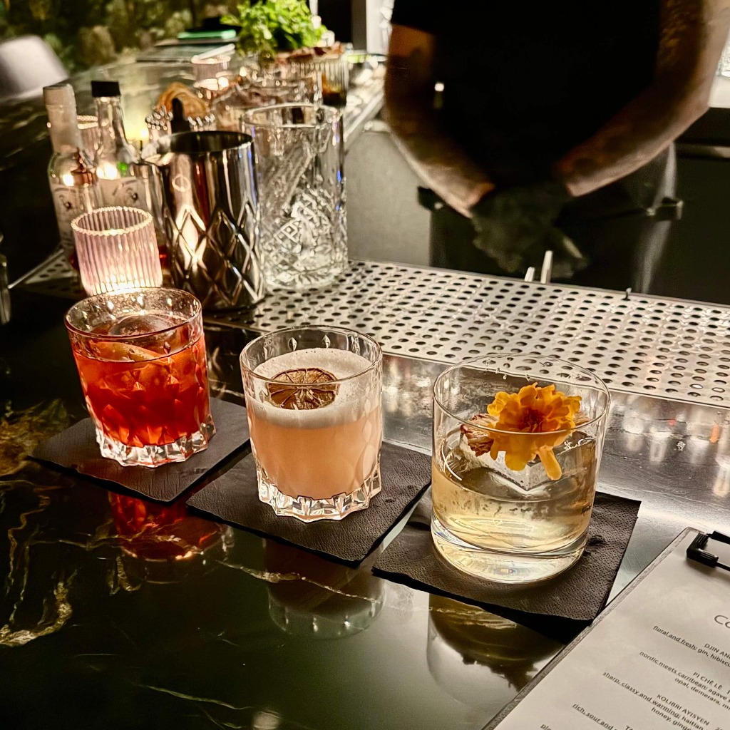 three colorful cocktails sitting on a bar side by side