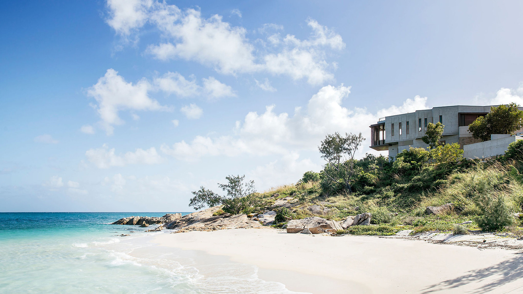 A private beach at The House on Lizard Island Resort, with clear blue skies and fluffy clouds creating a serene atmosphere.