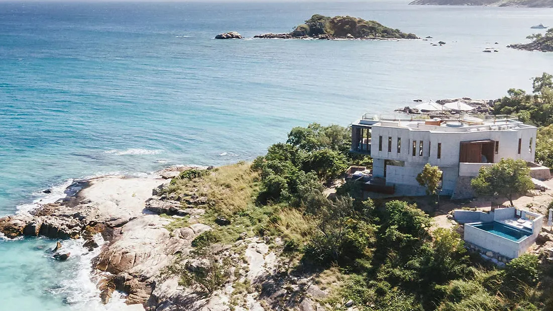The House exterior at Lizard Island Resort with pool on rocky cliff overlooking turquoise sea. Lush greenery surrounds, serene island visible in background under clear sky.