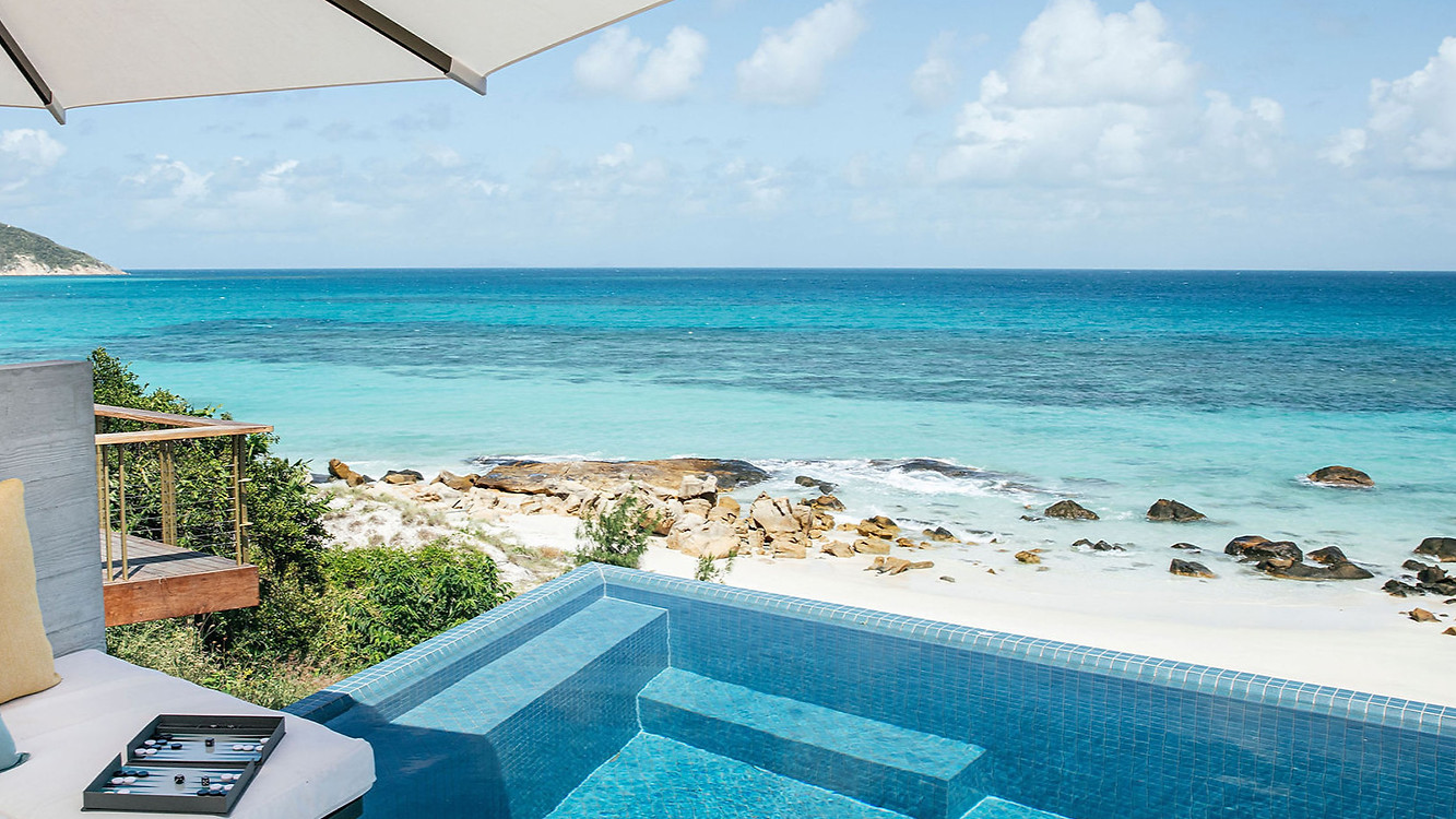 The House Lizard Island pool overlooking private beach with cushions under a large umbrella, under a blue sky