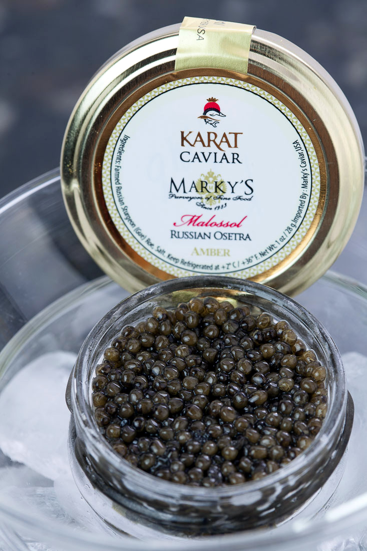 An open jar of Karat Russian Ossetra caviar beside its branded tin