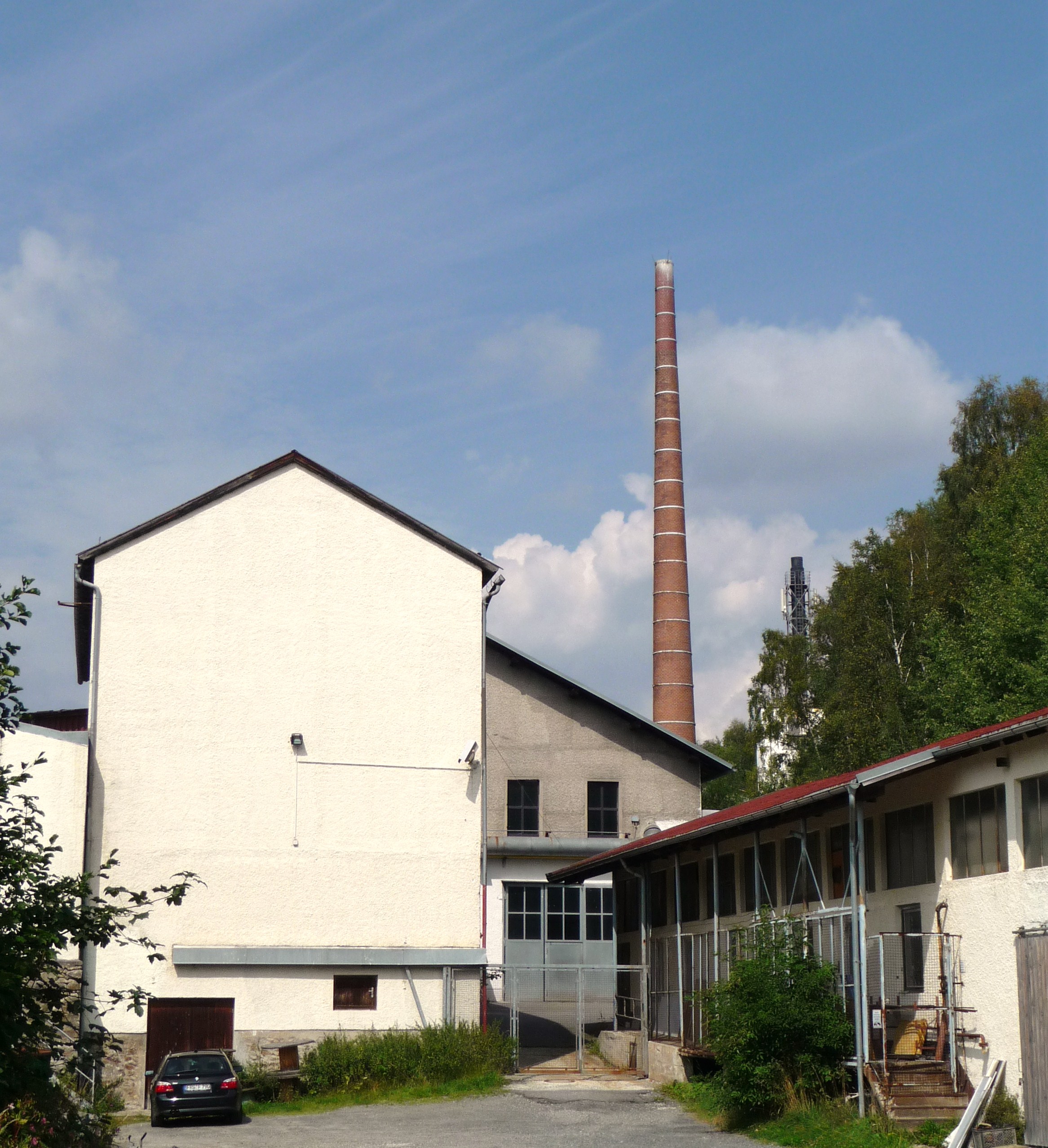 A historical SPIEGELAU crystal-glass factory building with a tall brick chimney